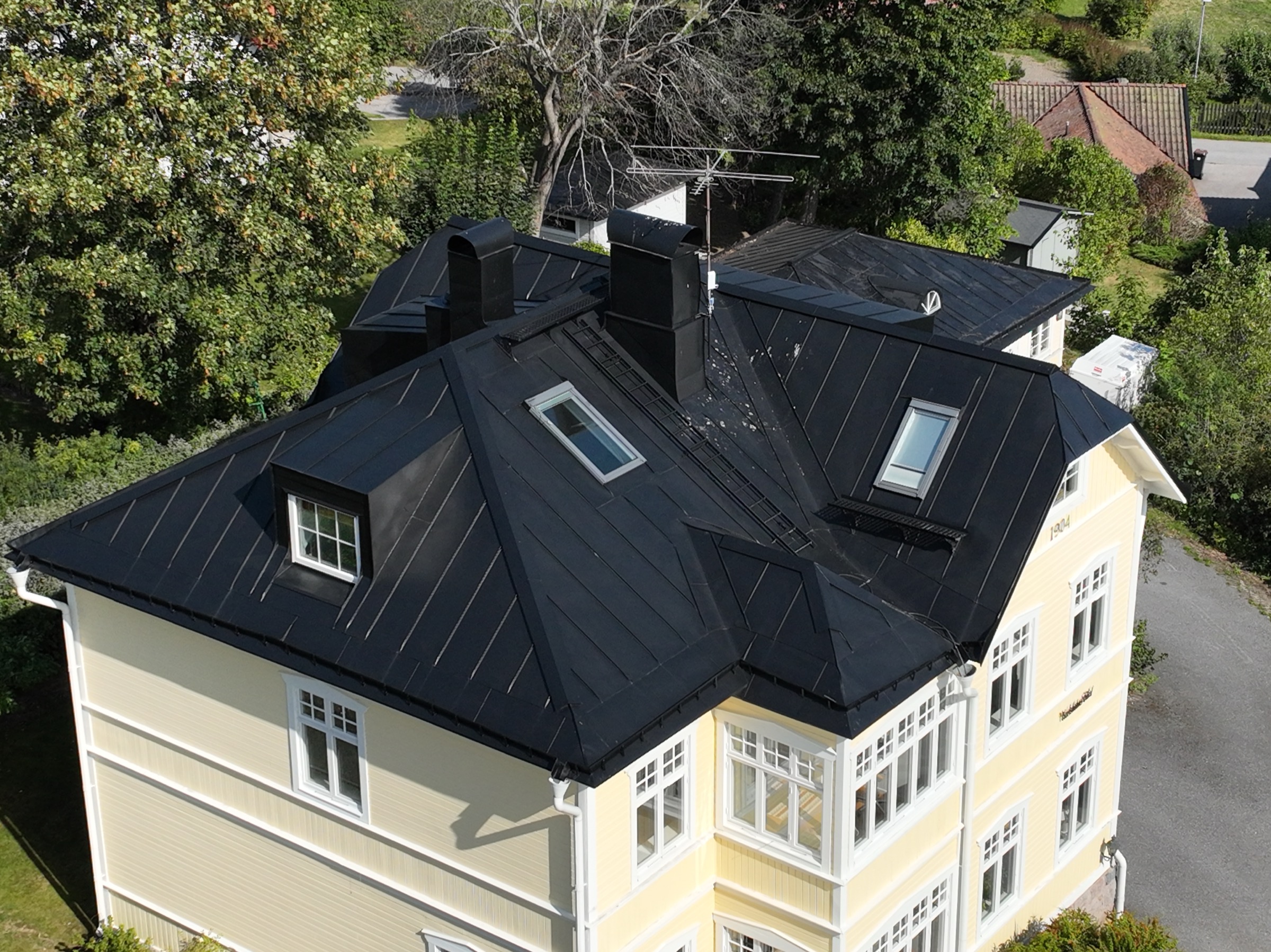 Svart falsat plåttak på gul villa — monterat av Arbetslag Bygg